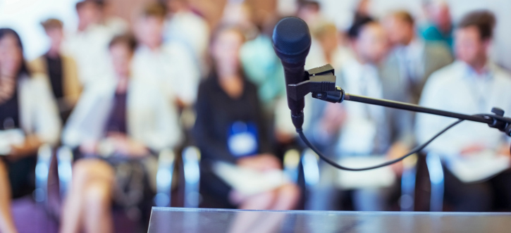 Close-up of microphone and transparent lectern with audience seen in blurred background